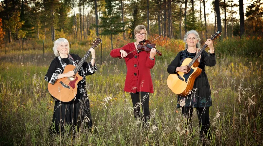 The Caleigh trio standing in a field holding their instruments